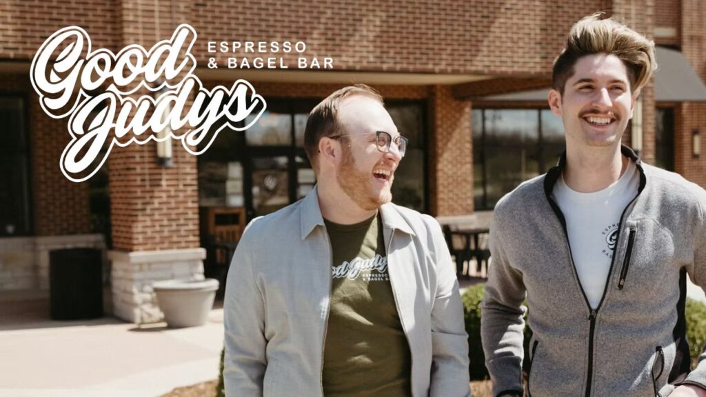 Good Judys Owners, Dakota and Jeff Thomas-Wilhelm, in front of their newly opened brick and mortar coffee shop. The logo of "Good Judys Espresso & Bagel Bar" to their left.